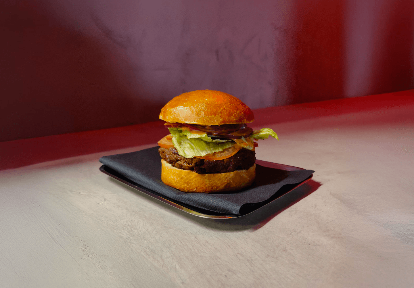 The classic burger served on a tray with a sleek, modern presentation under warm red lighting